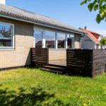 Ein Haus mit Holzterrasse und Grünfläche. Im Hintergrund steht ein weiteres Haus.