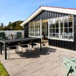 Terrasse mit Tisch, Stühlen und Grill neben einem Haus mit großen Fenstern.