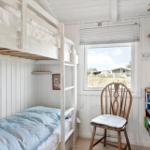 Kinderzimmer mit Doppelstockbett, Stuhl und Bücherregal. Fenster zeigt Außenbereich.