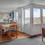 Dining room with table, chairs, and kitchen area. Large windows with view outside.