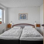 Two beds with white covers, window with view of field, wall pictures and wooden shelves.