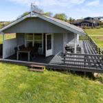 Holzveranda mit Grill und Tisch. Haus mit Dach und Antenne. Grünfläche im Hintergrund.