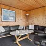 Wohnzimmer mit Holzwänden, schwarzen Ledersofas und ovalen Tisch.