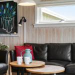 Black leather sofa with red cushions, wooden tables, and wall art on wood paneling.