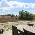 Deck with table and chairs, view of meadows and trees under blue sky.