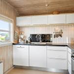 Kitchen with white cabinets, dark countertop, and wooden walls. Window with view outside.