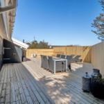 Holzterrasse mit Tisch, Stühlen und Liegen. Umgeben von Holzzaun und Bäumen.