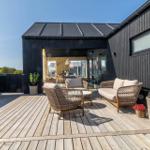 Terrasse mit Sitzgelegenheiten und Blick in das Haus. Holzdeck und schwarze Fassade.