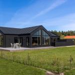Moderne schwarze Villa mit großem Garten und Terrasse mit Tisch und Stühlen.