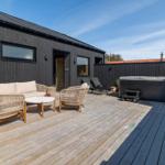 Terrasse mit Sofa, Stühlen und Whirlpool. Schwarzes Haus mit Holzdecke.