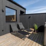 Terrasse mit zwei Liegestühlen, Holzboden und Whirlpool. Schwarze Holzwand und Fenster sichtbar.