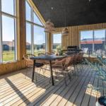 Terrasse mit Esstisch, Stühlen und Grill. Große Fenster, Holzboden und Pflanze.