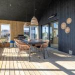 Terrasse mit Esstisch, Stühlen und Grill. Schwarze Holzwände und Holzdielen.