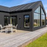 Moderne Villa mit Holzterrasse und großem Glasbereich. Außentisch mit Stühlen.