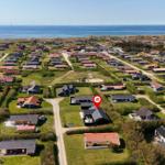 Aerial view of a coastal village with houses, greenery, and wind turbines near the sea.