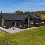 Moderne schwarze Villa mit großem Holzdeck und Garten. Große Fenster und Terrasse.