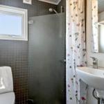 Badezimmer mit Dusche, Toilette und Waschbecken. Fenster und Blumenvorhang sichtbar.