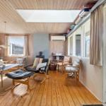 Wohnzimmer mit Holzboden, Sofa, Sessel und Terrassentür. Decke mit Dachfenster und Bücherregal.