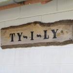 Holzschild mit der Aufschrift TY-I-LY an einer weißen Ziegelwand.