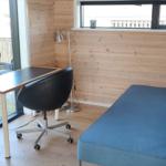 Ein Raum mit Schreibtisch, Stuhl und Sofa. Holzwand und Fenster.