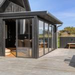 Terrasse mit Glaswand und Sitzgelegenheiten vor einem Haus mit dunklem Holzverkleidung.