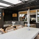 Terrasse mit Sitzgruppe, Esstisch und Blick ins Haus. Holzwände und offene Küche.
