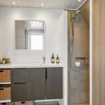 Badezimmer mit Dusche, Waschbecken und Spiegel. Holz- und Steinoptik.