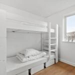 Ein Schlafzimmer mit weißen Doppelstockbetten und einem Fenster mit Blick auf Bäume.