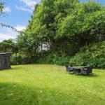 Garten mit Rasenfläche, Sitzgruppe und Holzschuppen. Umgeben von Bäumen und Sträuchern.
