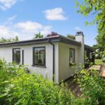 Ein weißes Haus mit dunklen Fensterrahmen und einem Gartenweg mit Holztisch.