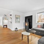Wohnbereich mit grauem Sofa, Kamin und Holzboden. Durchgang zur Essnische mit Tisch und Stühlen.