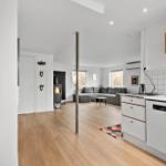 Küche mit weißen Schränken und Wohnbereich mit grauem Sofa und Kamin.