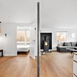 Wohnbereich mit Kamin und grauem Sofa. Durchgang zur Schlafzimmer mit Bett.