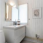 Bathroom with sink, mirror and toilet against white paneled walls.