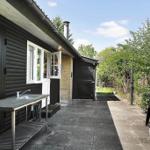 Outdoor area with grill, sink, and wooden house under blue sky.