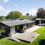 Black vacation house with terrace, garden, and pool. Surrounded by trees and greenery.