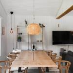 Dining room with wooden table, chairs, and TV. Large windows, fireplace, and ceiling beam.