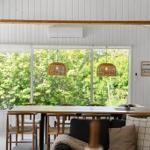 Dining room with wooden table, chairs, and view of green trees through large windows.