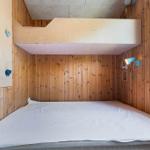 Room with wooden walls, lower bed, and upper bed with wall-mounted fixtures.