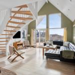 Wohnzimmer mit schwarzem Sofa, Holztreppe und großen Fenstern zur Aussicht.