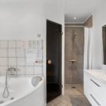 Badezimmer mit Badewanne, Dusche und Waschtisch. Weiße Fliesen und moderne Einrichtung.