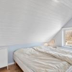 Schlafzimmer mit Dachschräge, Bett, kleinem Schrank und Fenster.
