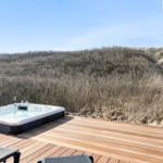 Hochwertige Whirlpool-Lounge auf Holzterrasse mit Blick auf Dünenlandschaft.
