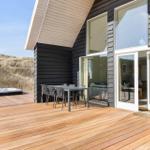 Terrasse mit Sitzgruppe und Whirlpool neben modernem Haus mit großem Fenster.