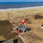 Haus mit Terrasse an der Nordsee, umgeben von Dünen und Strand.