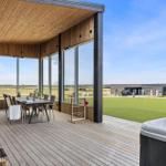 Terrasse mit Grill, Tisch und Sitzgelegenheiten. Blick auf grünes Feld und Nebengebäude.