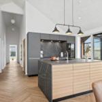 Moderne Küche mit Insel, dunkler Arbeitsplatte und Holzfronten. Helle Wände und Holzboden.