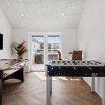 Raum mit Foosballtisch und Airhockeytisch, TV und Balkontür.