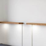 Zwei hölzerne Regale an der Wand über einem Bett mit integrierten Lichtern.