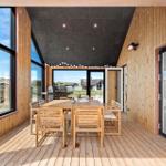 Terrasse mit Holztisch, Stühlen und Grill. Große Fenster mit Blick auf Strand.